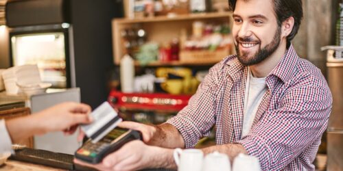 Smiling dark-haired bartender serves woman standing near bar counter in cafe, paying for the order